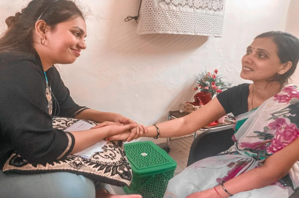 a woman in jeans and kurta holding the hand of another woman wearing a saree--palliative care