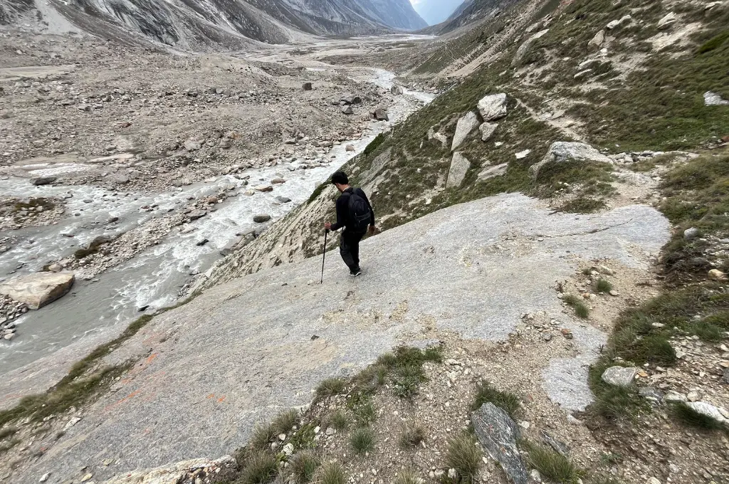 a man descending from a large boulder in a rocky and mountainous landscape with a river flowing on the left--conservationists