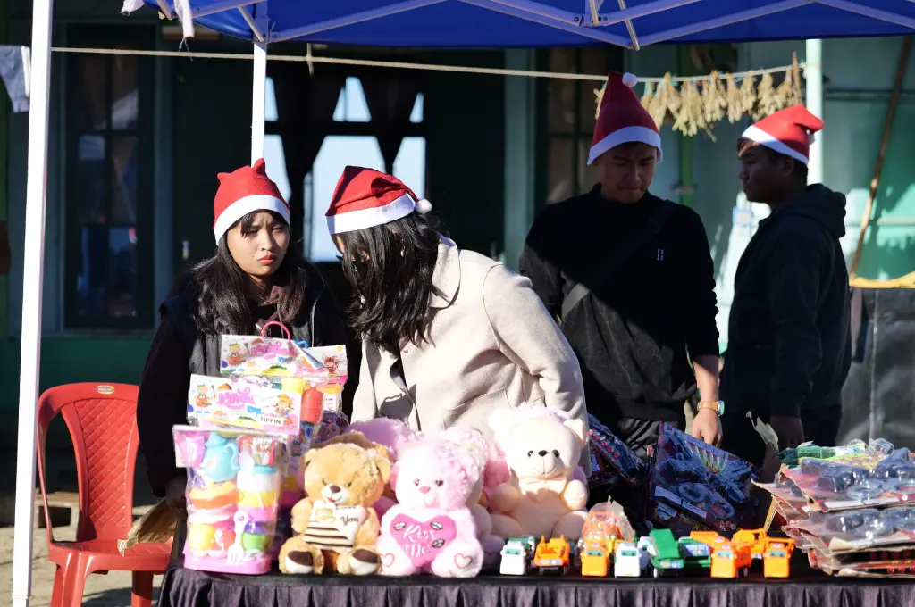 four people, two men and two women, in santa hats standing behind a counter selling teddy bears and a variety of plastic toys--crowdfunding in Mizoram