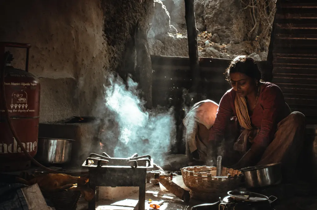 a woman sitting on the floor of her kitchen and preparing food, with an Indane LPG cylinder to her right--electric cooking