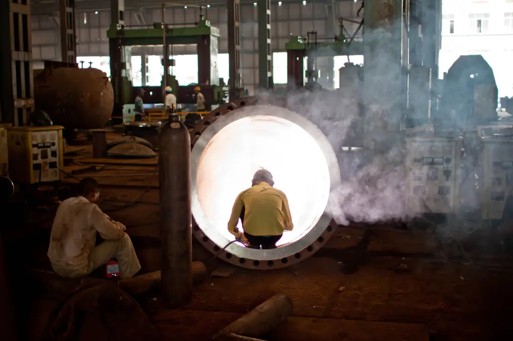 a factory floor with several workers, one of whom is welding a large metal tube--energy transition