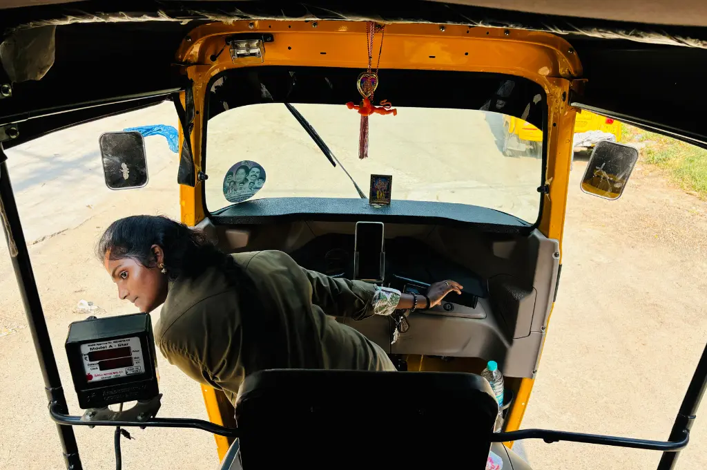 a woman driving an auto rickshaw leaning out of the auto to look at something--women auto drivers