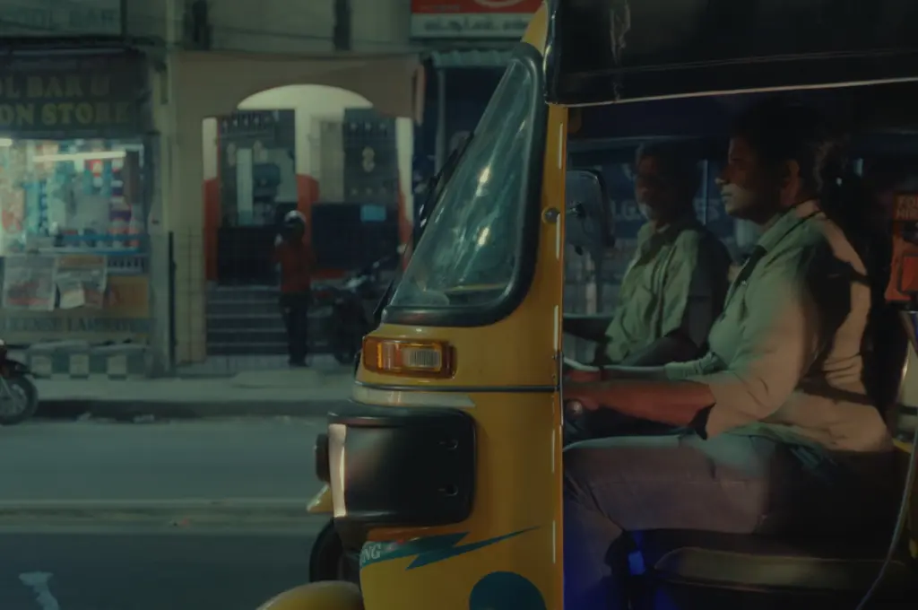 a woman drives an auto rickshaw as a man looks at her--women auto drivers