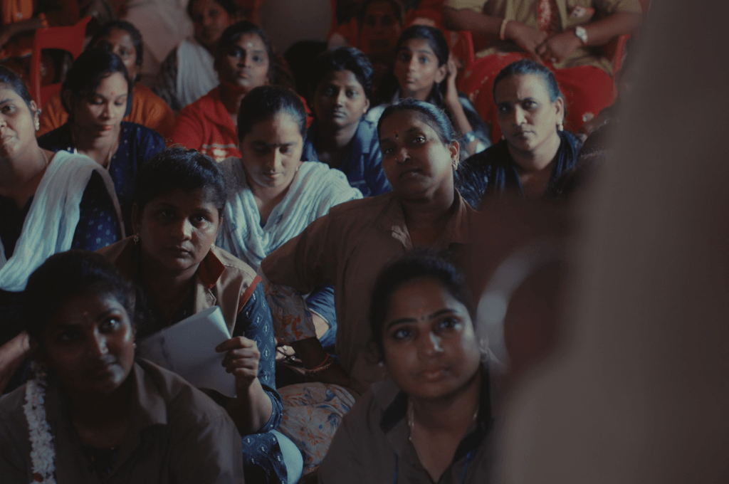 a group of women seated on the floor, watching a speaker addressing tm
