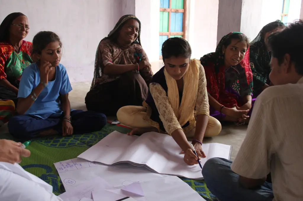 a group of women and young girls sitting on the floor with large sheets of paper spread out in front of them; one of the girls appears to be writing something--Community stewardship