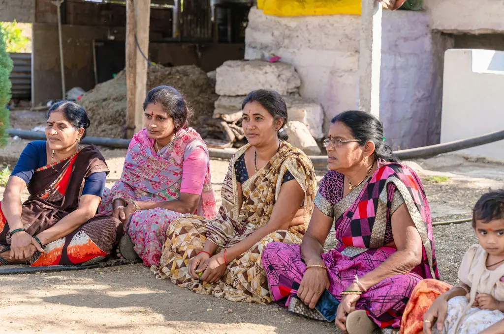 four saree-clad women and a small child sitting on the ground--theory of change