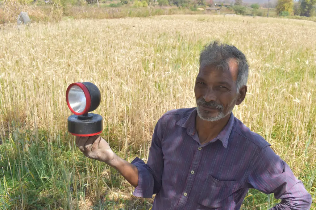 an elderly man standing in a field and holding up a light in his right hand--pench tiger reserve