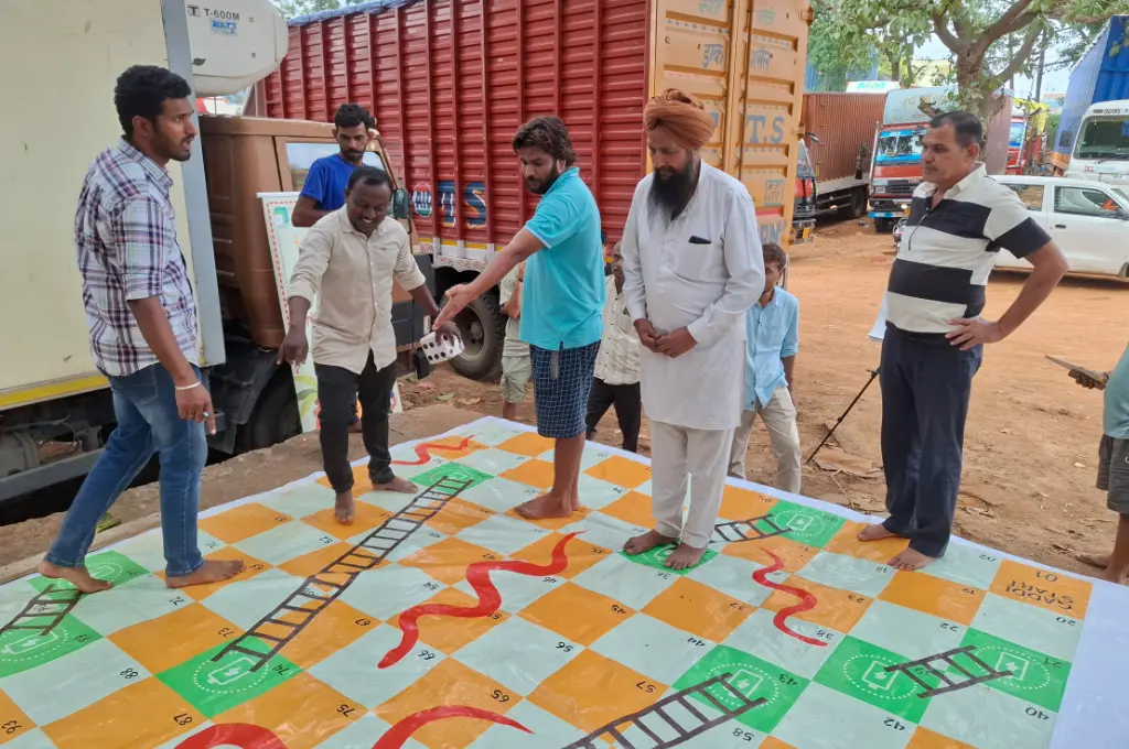 a group of people playing a game of snakes and ladders on a life-sized board et up on the ground--unorganised sector India