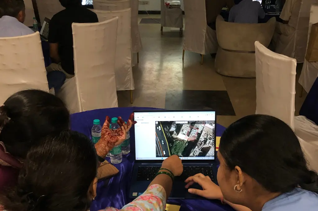 three women sitting in front of a laptop look at a street-view map--urban villages in Delhi