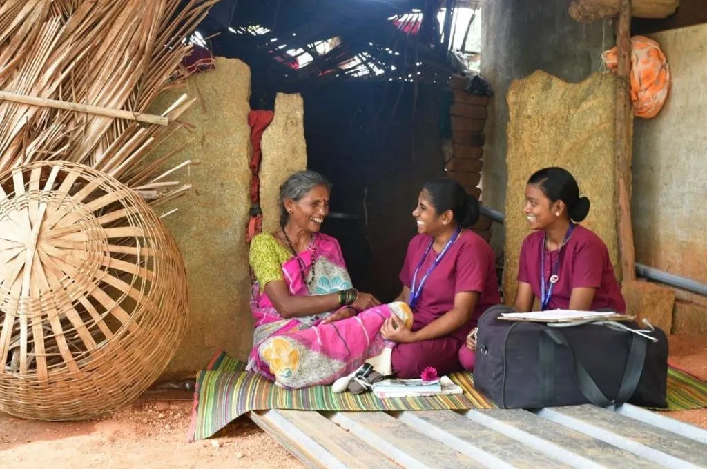three women sitting and talking on a mat with a large basket to their right--palliative care