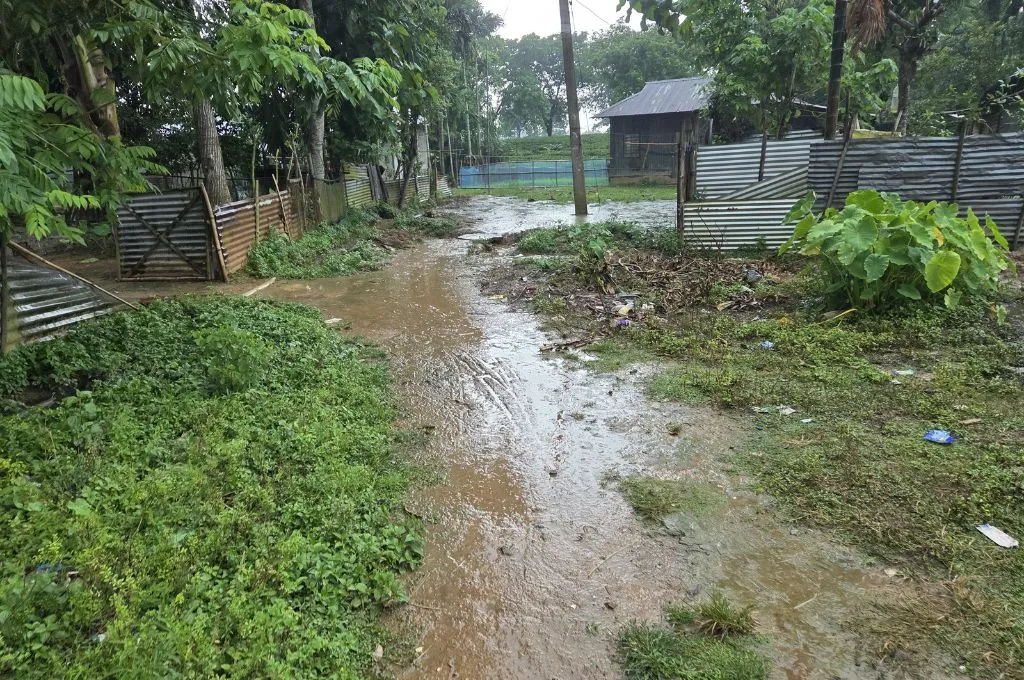 a muddy road with patches of green and some houses in the distance--tea estates