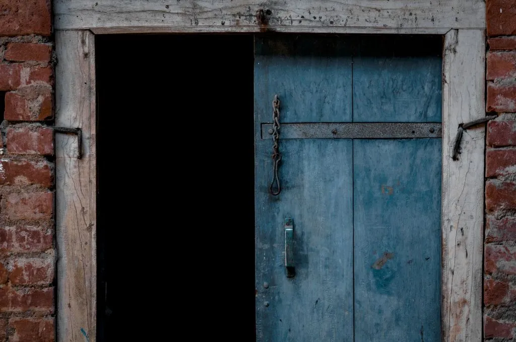 A blue door partially opened and set in a weathered red brick wall, with a dark interior space behind it--social change