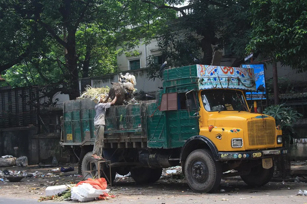 a man throwing waste in a big green and yellow truck parked on the roadside--waste management India