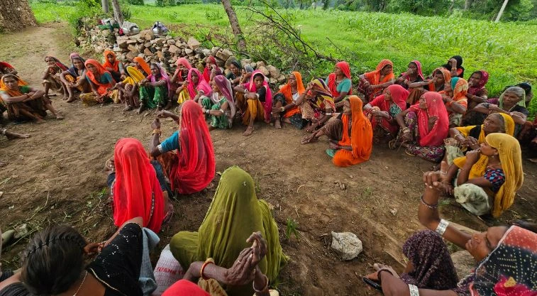a large group of women sitting on the ground next to a field--MGNREGA