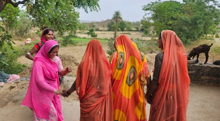 two women shaking hands and laughing while three others look on--MGNREGA