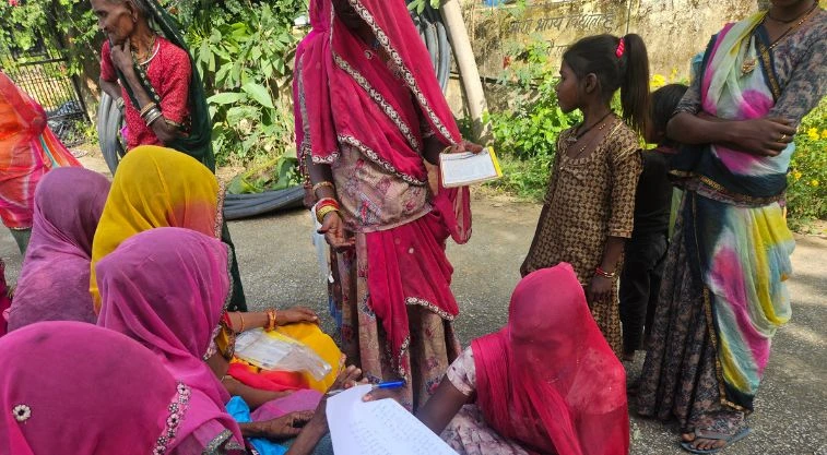 a group of women, some with their faces veiled, perusing a long list--MGNREGA