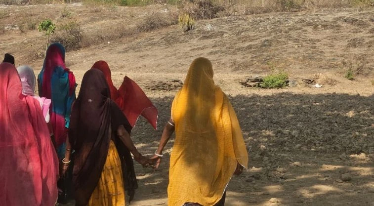 a group of women walking on unpaved ground; two of them are holding hands--MGNREGA