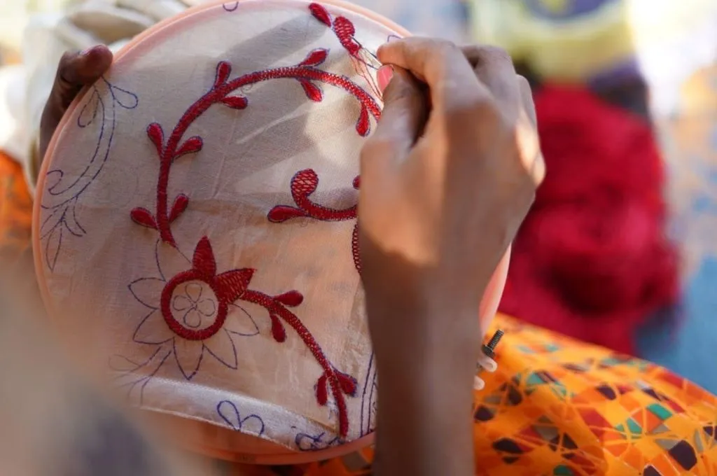 a close up of a hand embroidering a piece of white fabric--chikankari