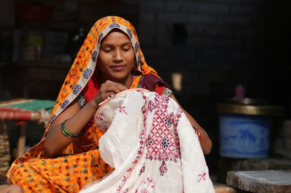 a woman in a bright yellow saree embroidering a piece of white fabric--chikankari