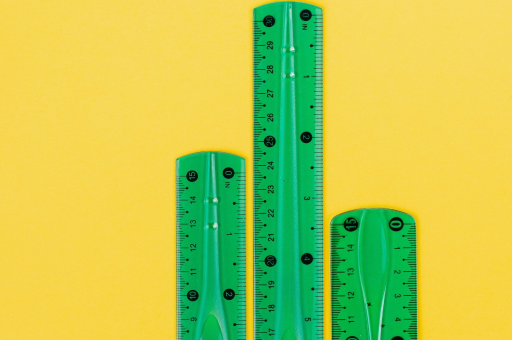 three green-coloured rulers of varying lengths against a yellow background--outcomes-based financing