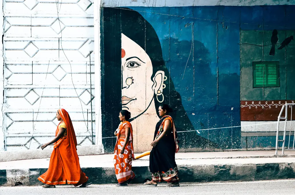 three women walk on a street past a large mural of a woman's face--cybercrime reporting