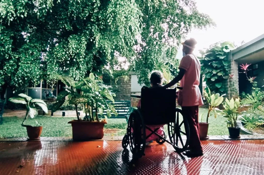 an old woman in a wheelchair, with a nurse standing next to her, looks out at a garden--hospice facilities