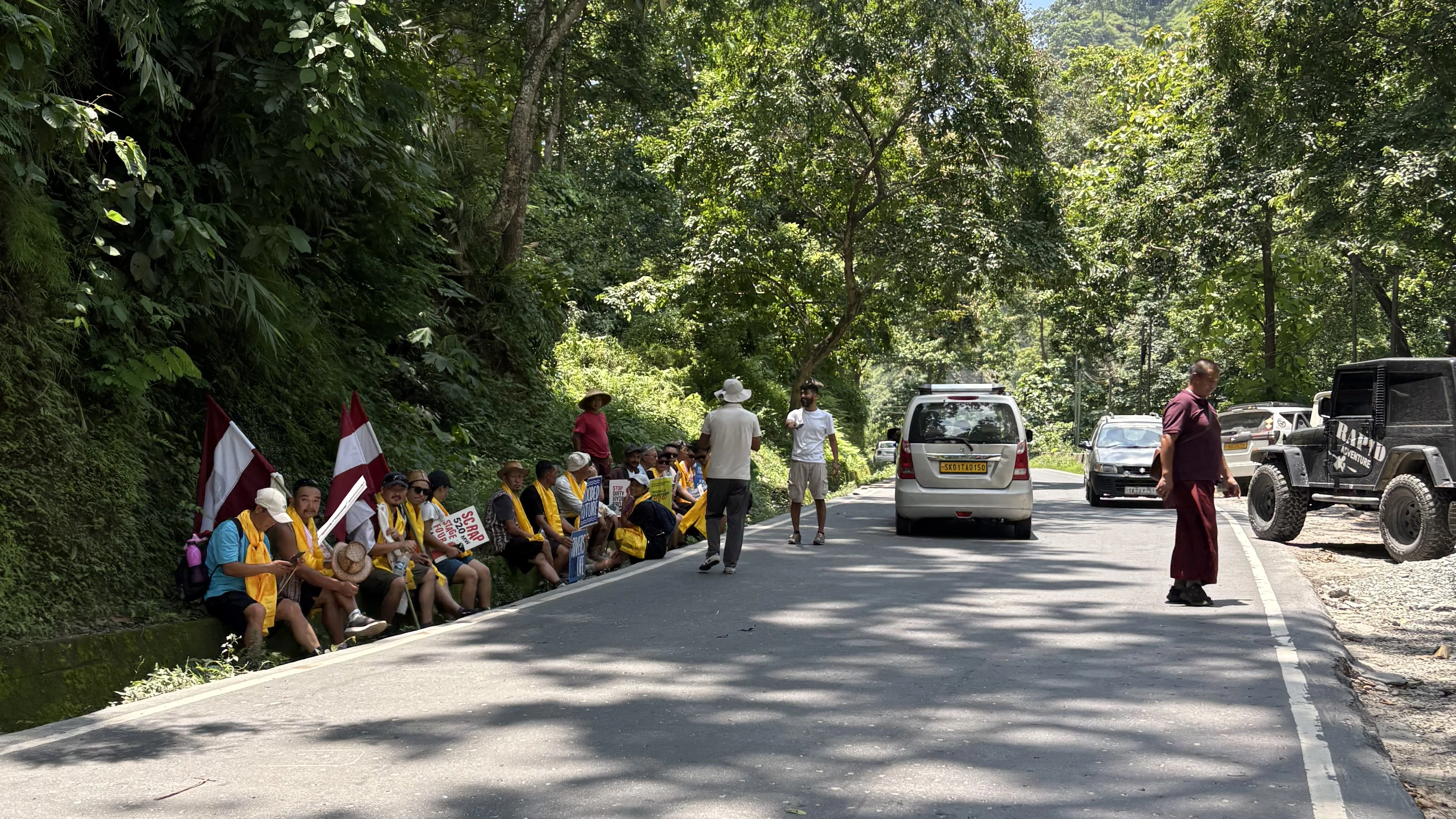 A group of people carrying flags marching alongside a road in single file--Teesta hydropower projects