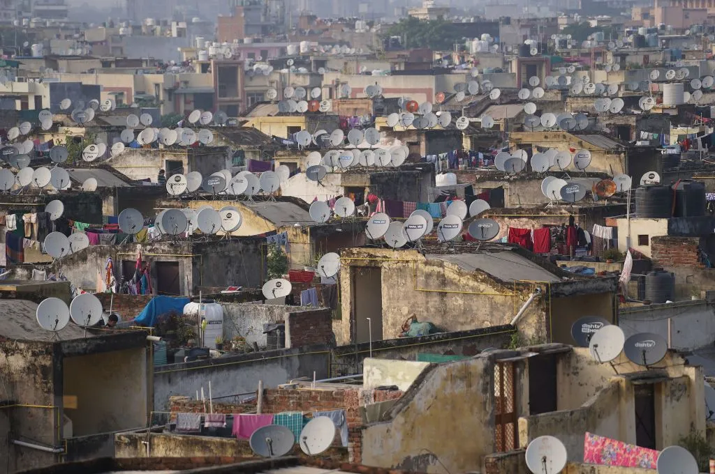Dense urban rooftops are covered with hundreds of satellite dishes, water tanks, laundry, and closely packed buildings--urban housing