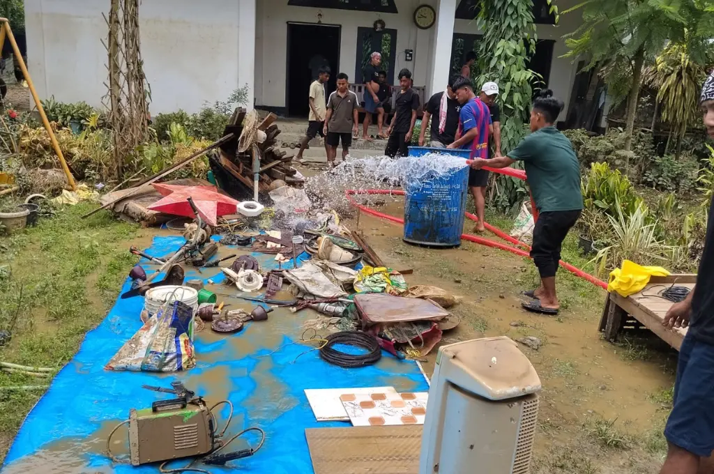 a man hosing down mud-covered items laid out on blue tarp--Nagaland floods