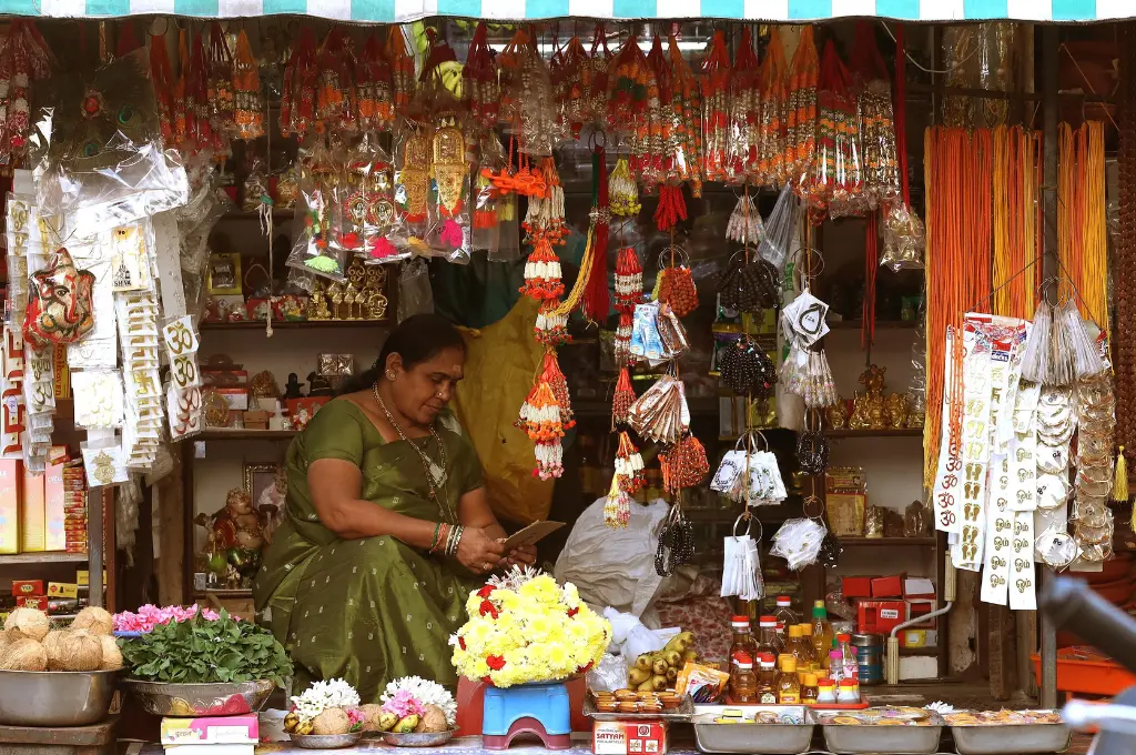 A woman in green saree sitting in her colourful street market stall, offering traditional Indian goods and decorations.-informal sector