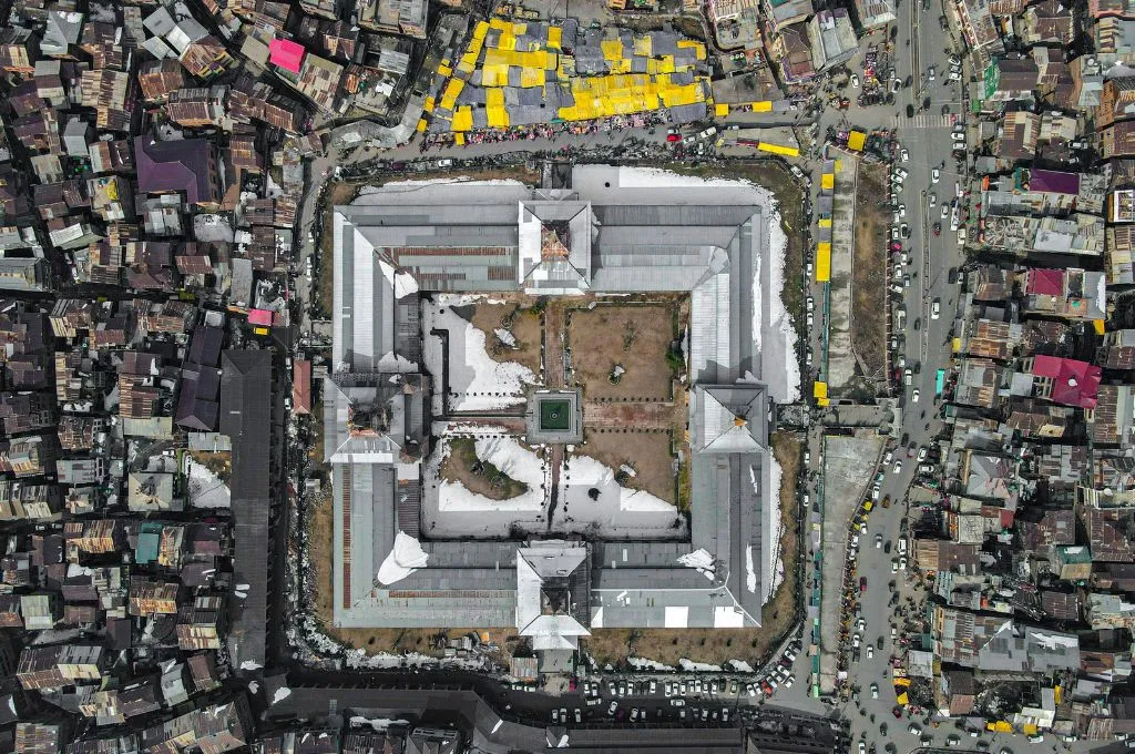 Aerial view of a large building with a rectangular courtyard, surrounded by densely packed buildings, busy streets, and market stalls--AI for social impact
