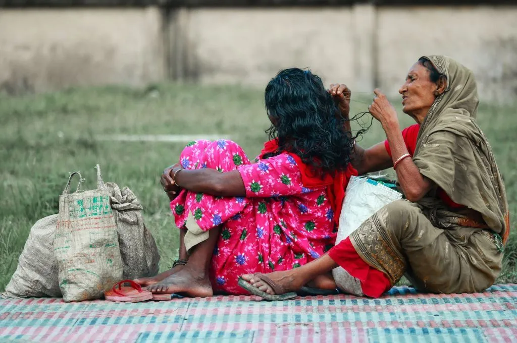 Two women sitting, with one of them massaging the other's head.