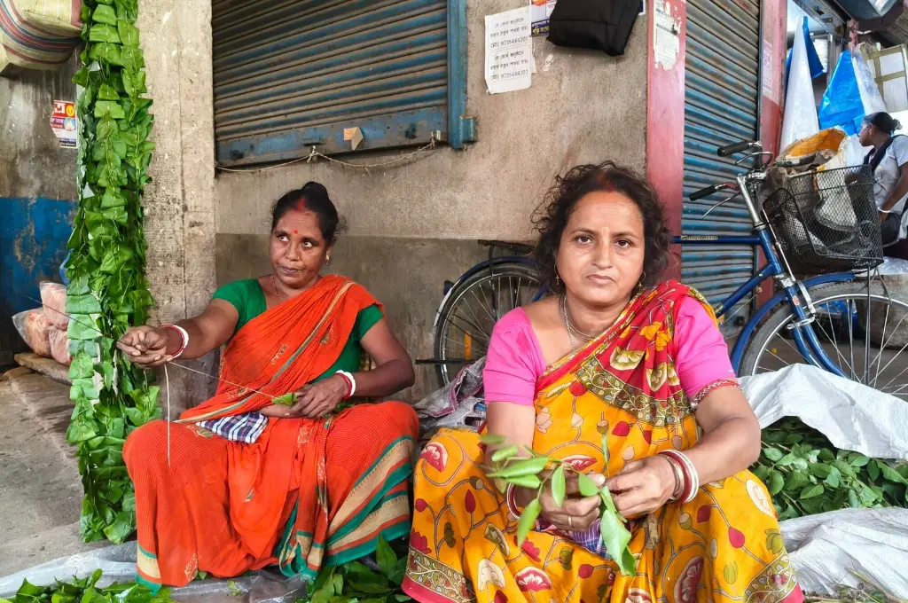 Two female flower sellers sitting in a street corner, threading bel leaves--SIR