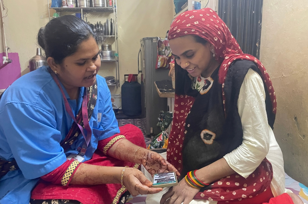 a healthcare worker wearing a blue shirt over her clothes showing a pregnant woman how to operate a chatbot--AI tools