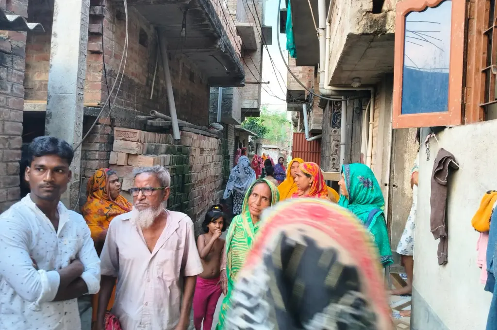 a group of people, some with their backs to the camera, standing in a crowded narrow street with brick homes--SIR