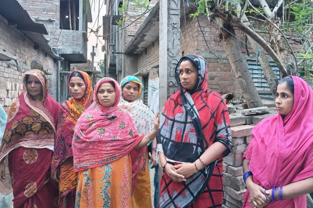 a group of women standing in a narrow street with several brick buildings--SIR