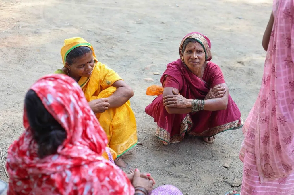 two women (facing the camera) squatting on the ground and talking to two other women (with their backs to the camera)--fertilisers