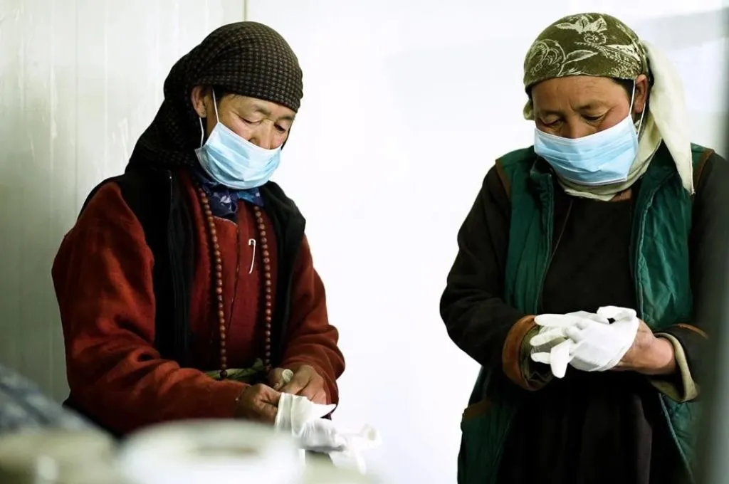 two women with their heads, mouths, and noses covered, and wearing gloves, making soap--goat milk soap