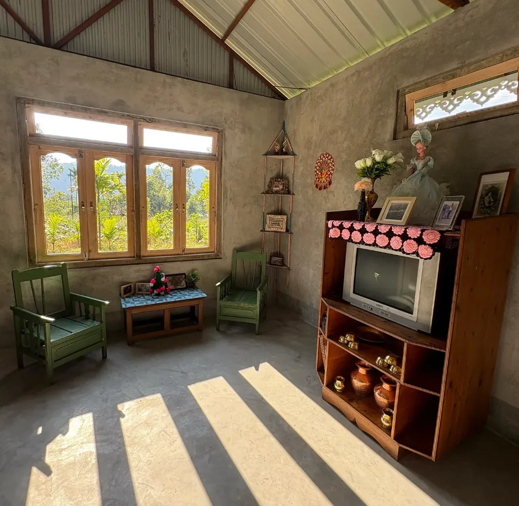 a bright sitting room with two chairs and an end table by a window and a television cabinet with a CRT tv and decorative items--photo archive