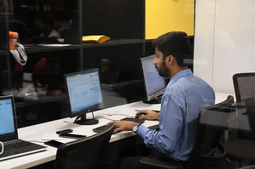 a man sitting at an open-plan desk working on a computer--managers