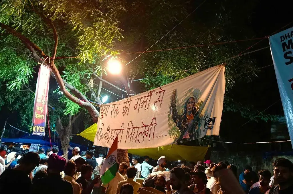 a large crowd during a nighttime protest holding up a banner--Delhi protests