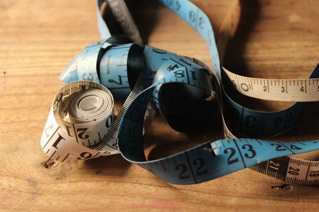 A blue and white measuring tape loosely coiled on a wooden table, with measurement markings and numbers visible--performance assessment