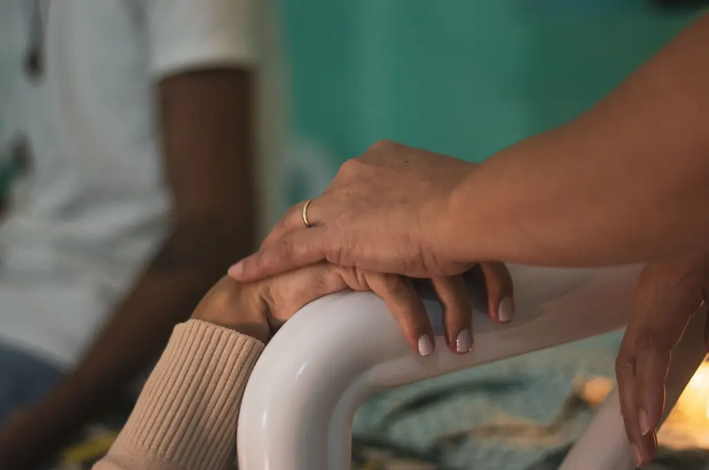 close-up of one hand placed on another on a hospital bed--palliative care