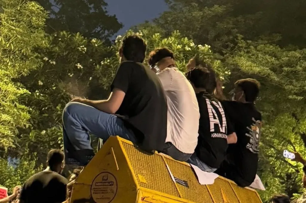three young men sitting on a yellow barricade during a protest--Delhi protest